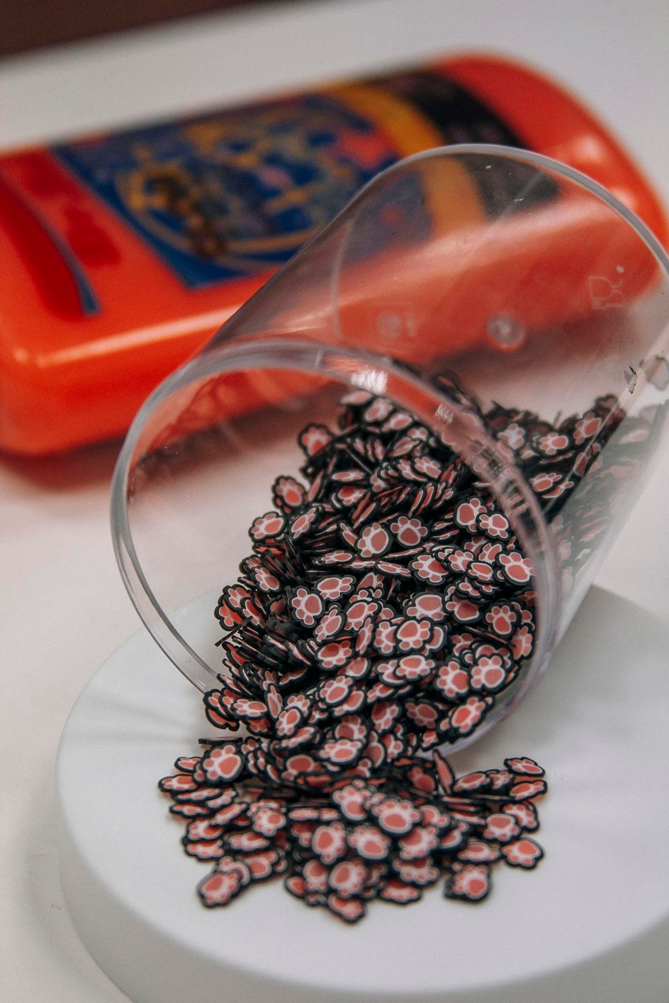 Charming paw-shaped beads spilling from a transparent cup onto a surface.